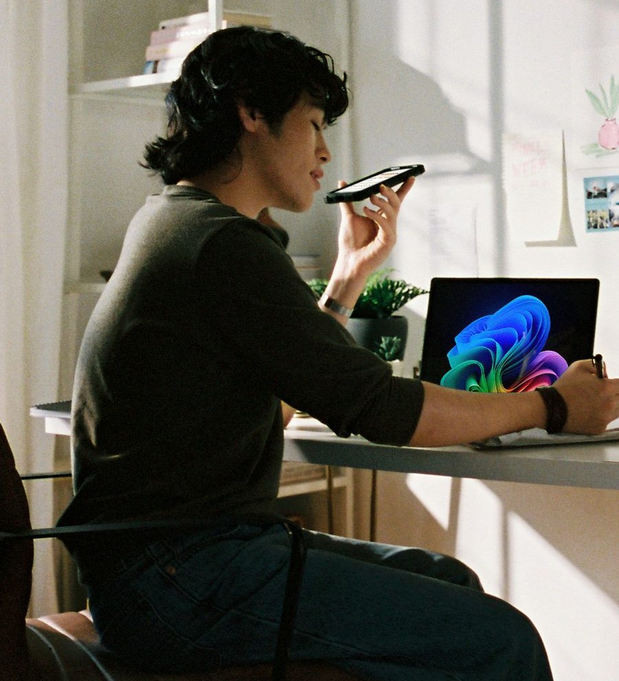 A writer at a sunlit desk, speaking a thought into their phone