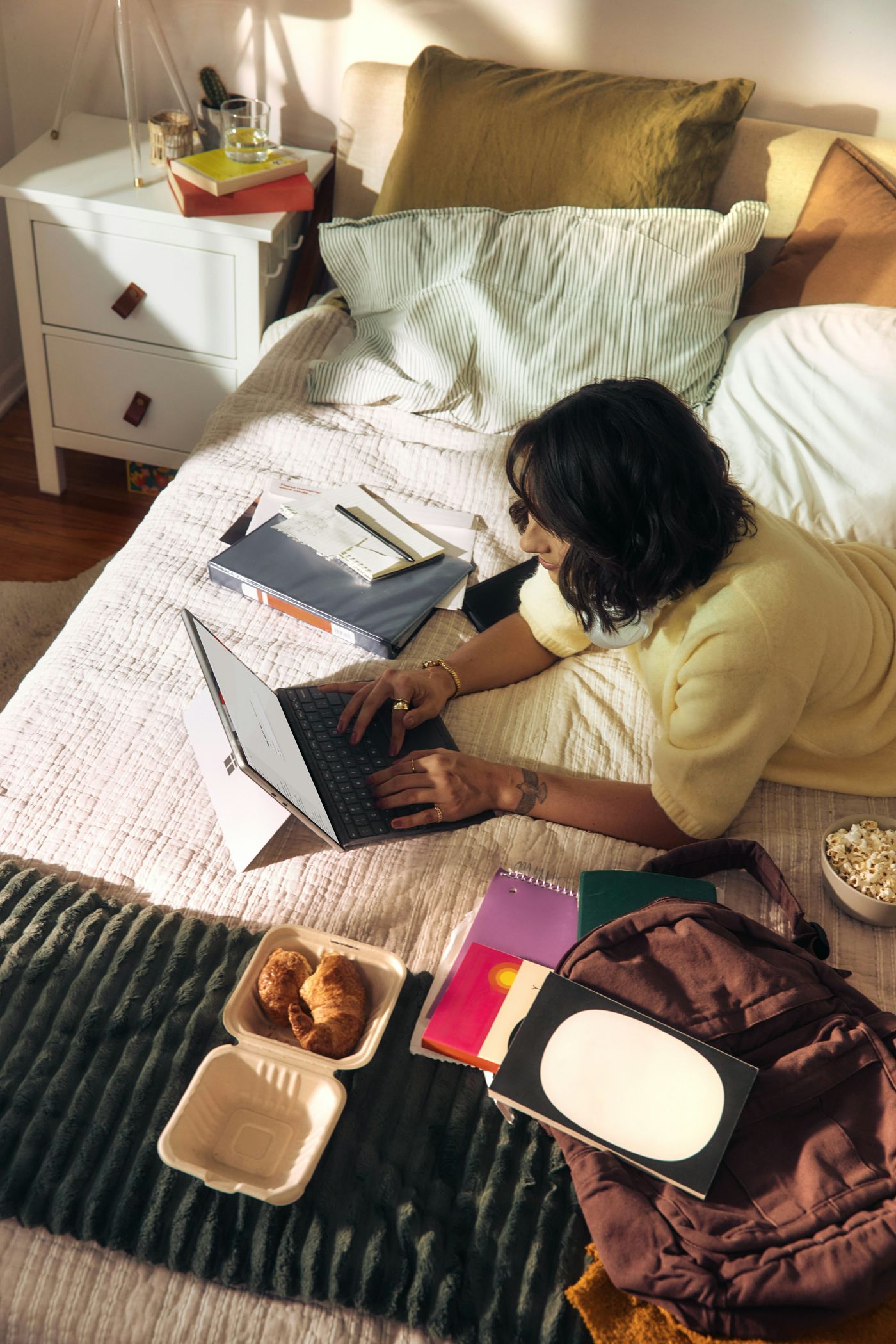 A writer typing from the comfort of her bed, notebooks around her